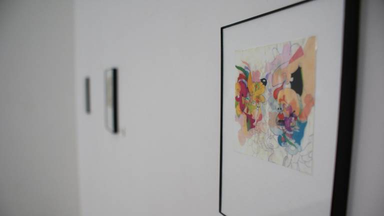 A piece of framed art hangs on a wall as part of an art gallery