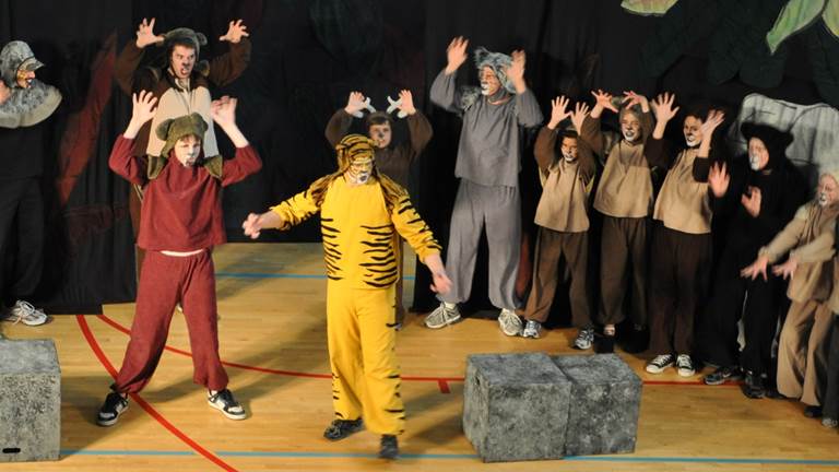 A group of students dressed in animal costumes perform a play on a stage