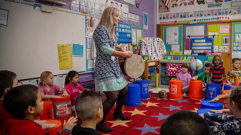  A teacher and students sitting in a circle playing the drums. 