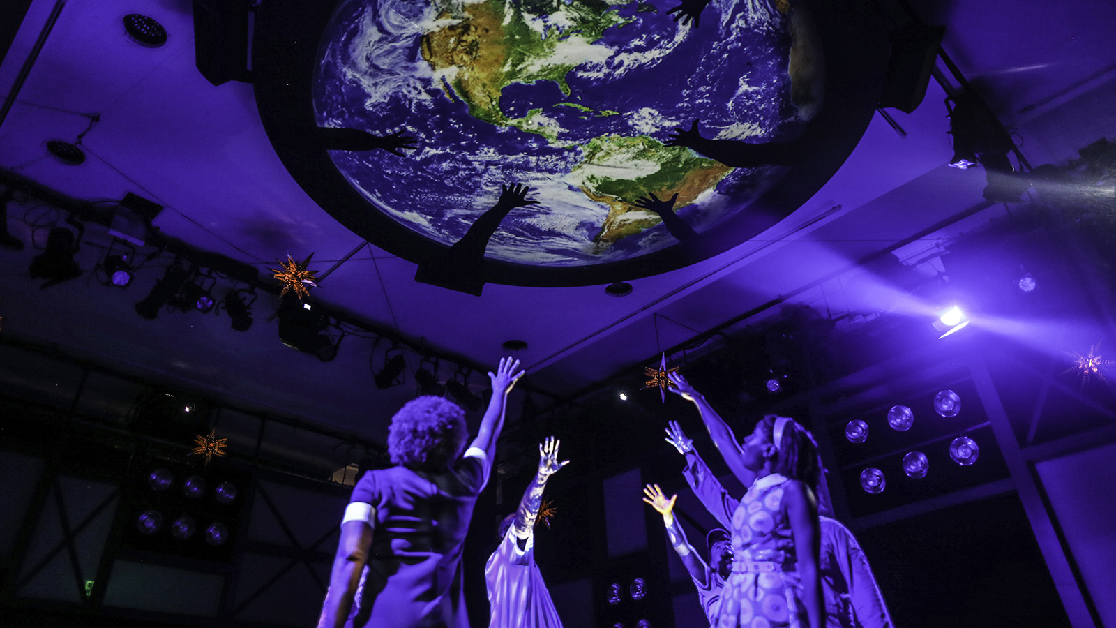 Actors reach up toward an overhead image of the earth in Earthrise
