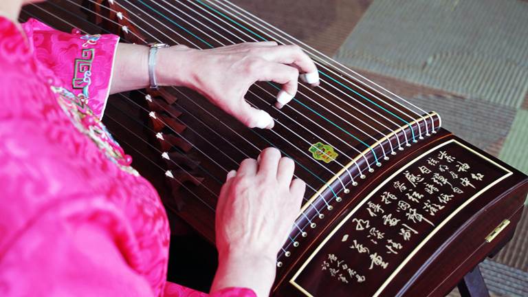 A musician plucking a stringed instrument called a guzheng.