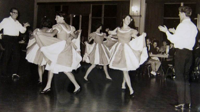 A black and white photo of people square dancing. 