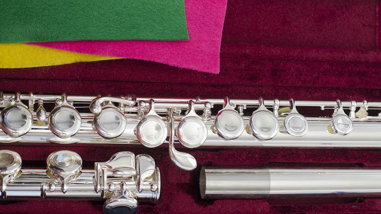 A silver flute in an instrument case. There are three cleaning pads in green, pink, and yellow laying next to the flute.  