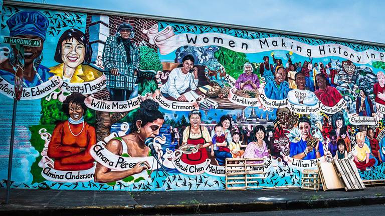 A colorful mural on the side of a building. The mural depicts women who made history in Portland.