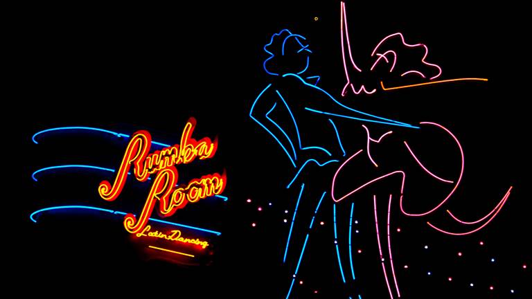 A neon sign with two dancers that says "Rumba Room Latin Dancing."