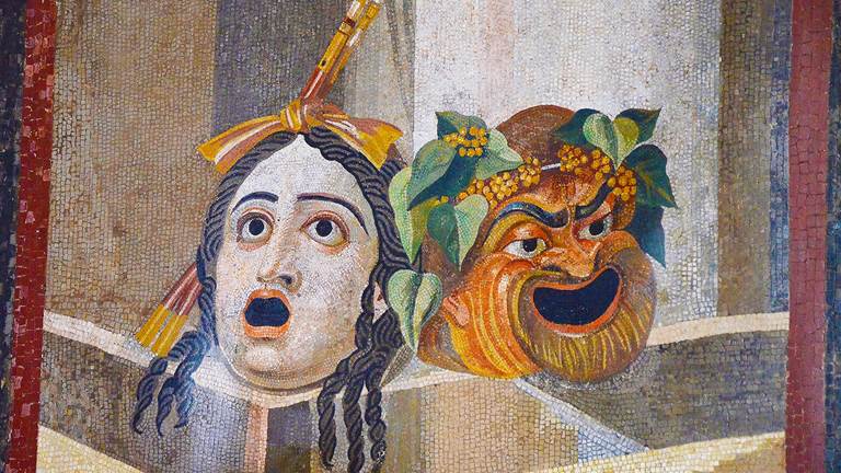   Mosaic tile art of two greek comedy and tragedy masks. The mask on the left has long hair in twists with its mouth wide open. The mask on the right has short hair with a leaf branch headband and is smiling.