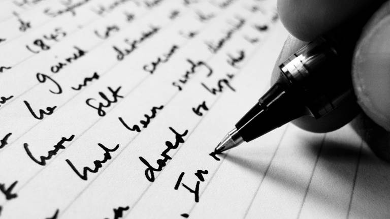 A close-up image of a hand writing with a felt-tip pen on lined paper. The image is in black and white.