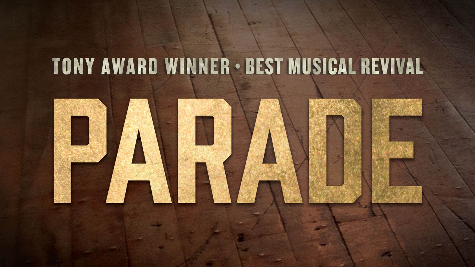 The word "Parade" in a large gold san serif font is in the middle of the photo. In much smaller font above it is "Tony Award Winner, Best Musical Revival". The background is a old dirty brown wood floor. 