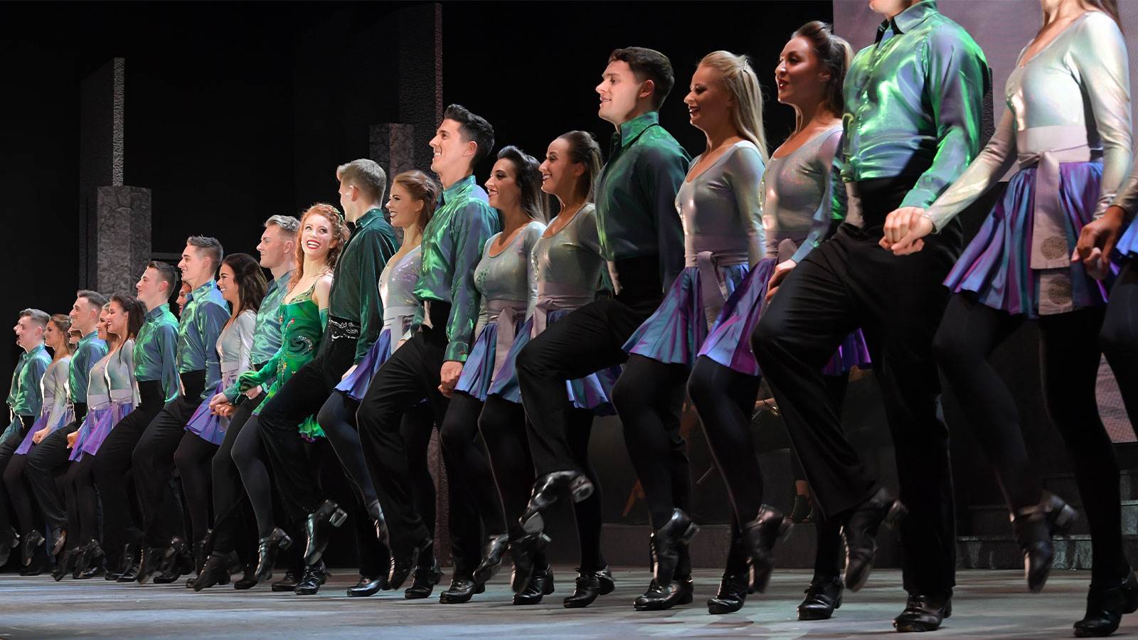 A line of over 20 Irish dancers in silver, green, and purple sparkly dance costumes. 